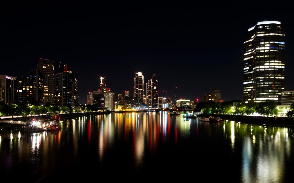 Nighttime view of the River Thames with modern Vauxhall and Nine Elms skyscraper cluster glowing in the background and the illuminated geometric facade of Millbank Tower prominent on the north bank.