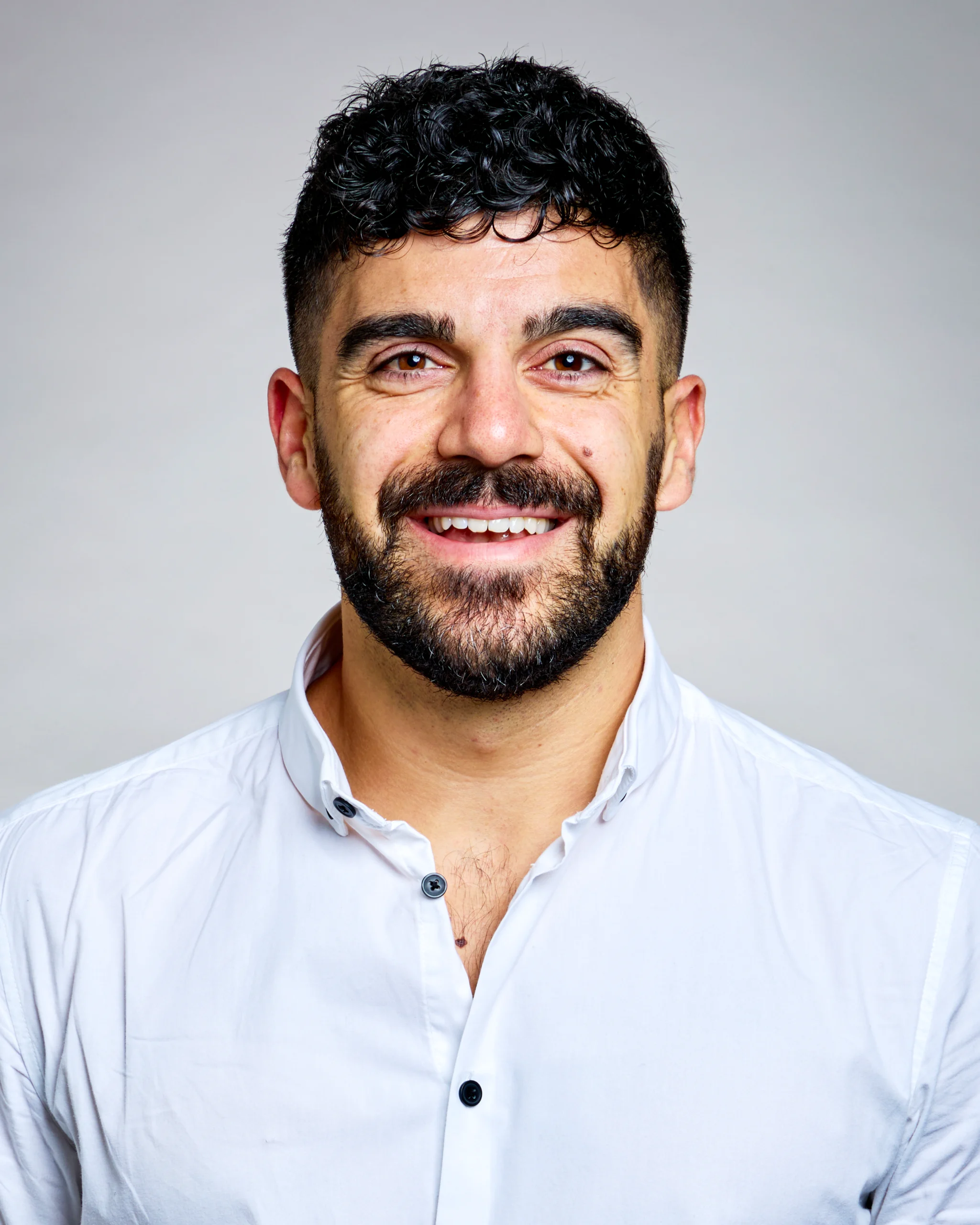 A bearded man with curly hair smiles broadly.