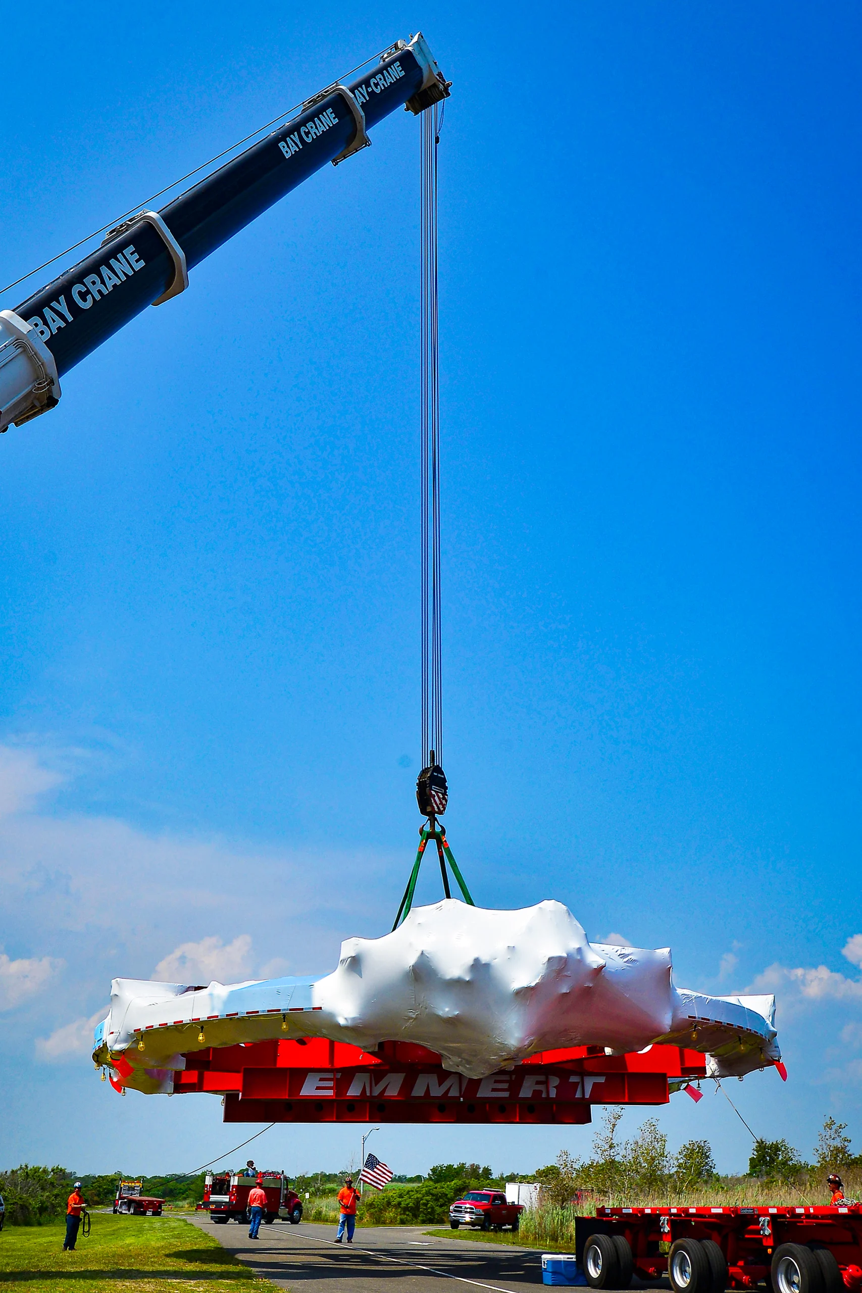 A large crane lifts a colossal magnetic ring mounted on a red frame as workers look on.