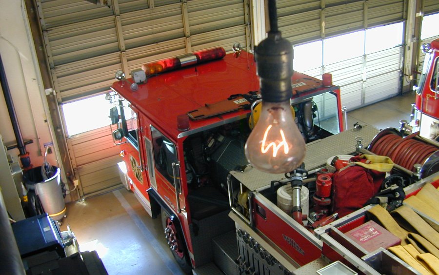 A carbon filament lamp handing from a pendant. The bulb is dirty and the filament glows a dim orange.