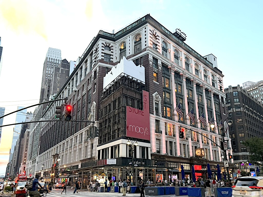 Macy's department store building in New York City, featuring a mix of modern and historic architecture, with a busy street scene and traffic lights in the foreground.