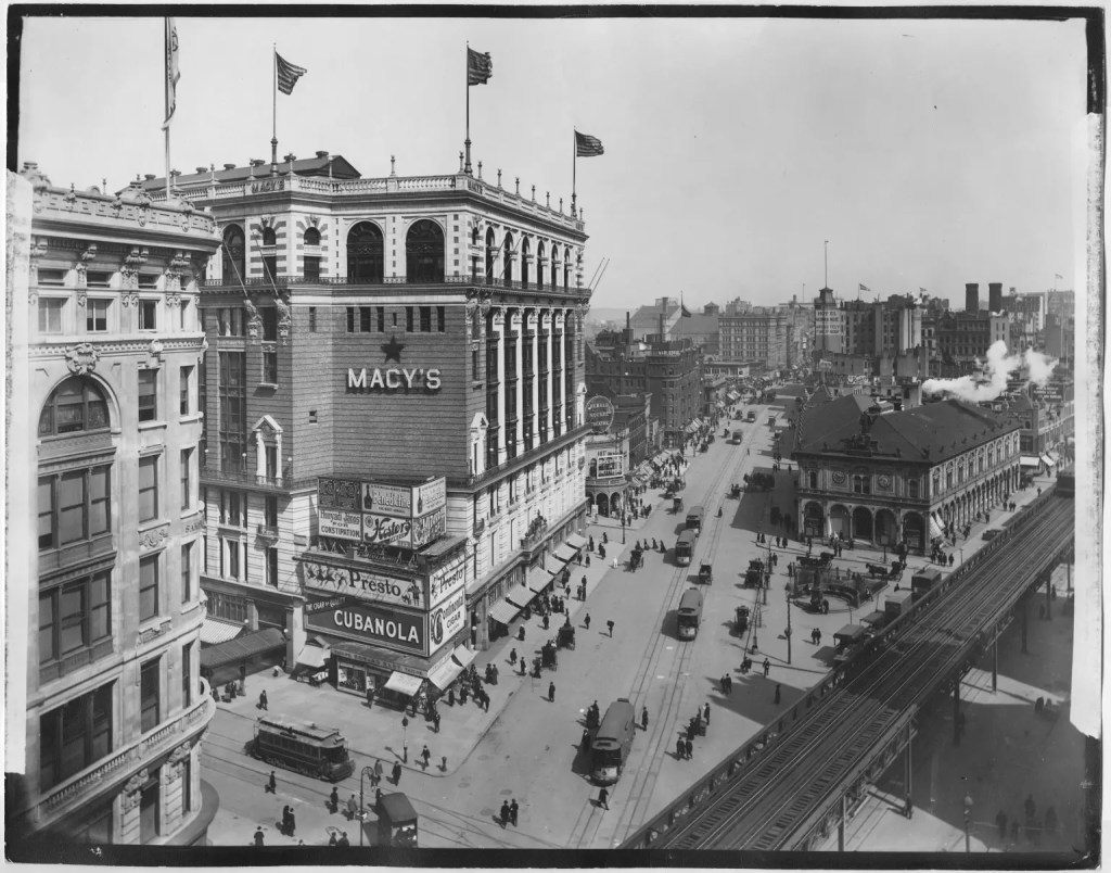 Historic black and white photograph of Macy's department store in New York City, showcasing streetcars and pedestrians in the bustling urban environment.