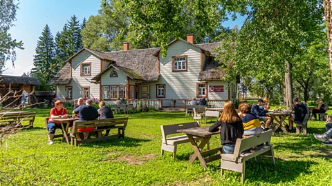 Martin Mark People sitting in a garden at picnic tables with a wooden farmhouse in the background (Credit: Martin Mark)