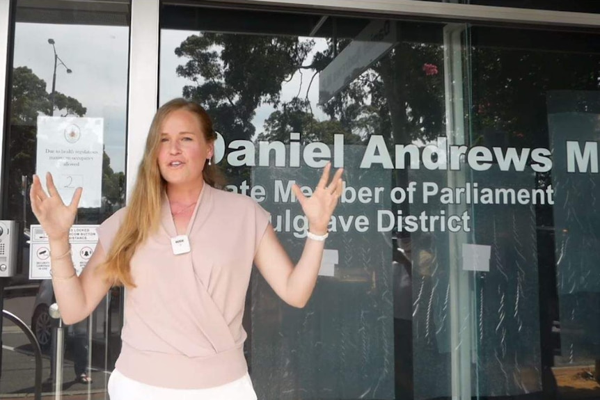 A woman in her early 30s raises her arms while giving a speech outside Dan Andrews' office