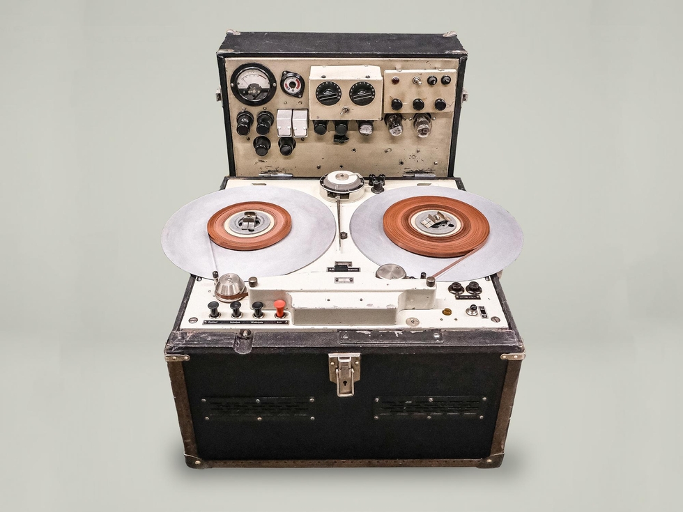 Color photo of a reel to reel tape recorder with a black case and multiple knobs and switches.