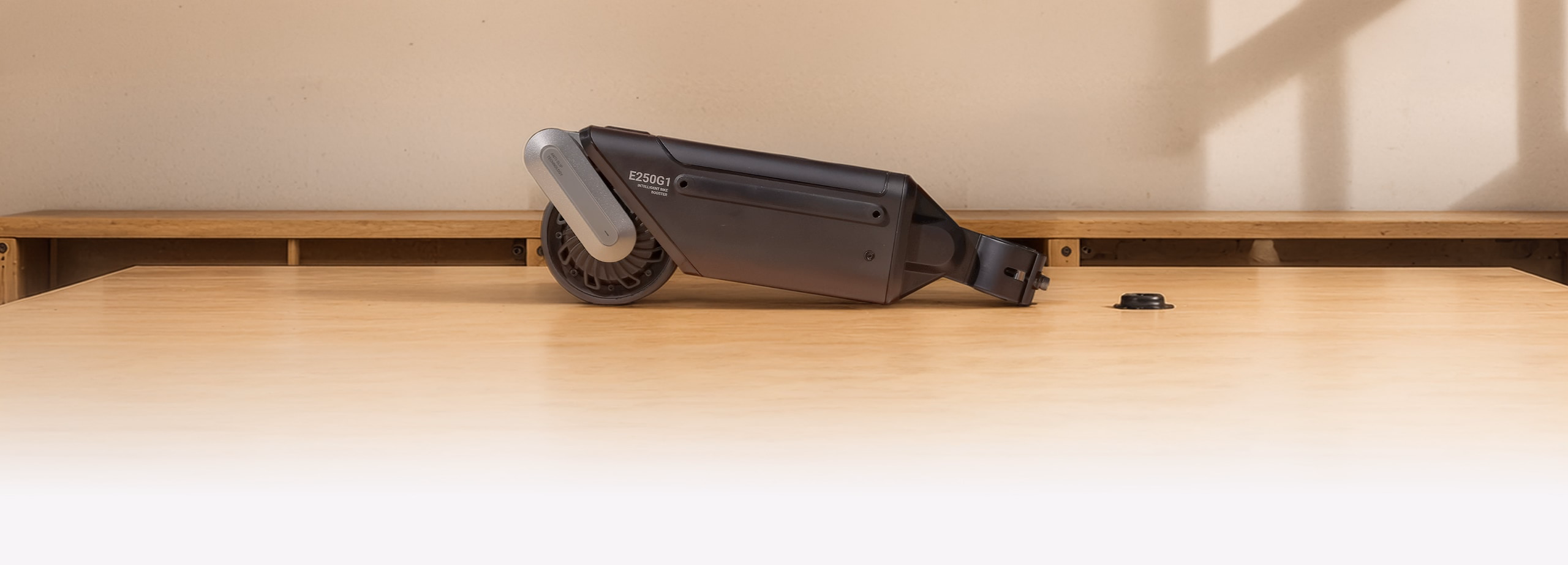 A Oxiis bike booster kit on a wooden tabletop, showing its compact design and drive wheel.