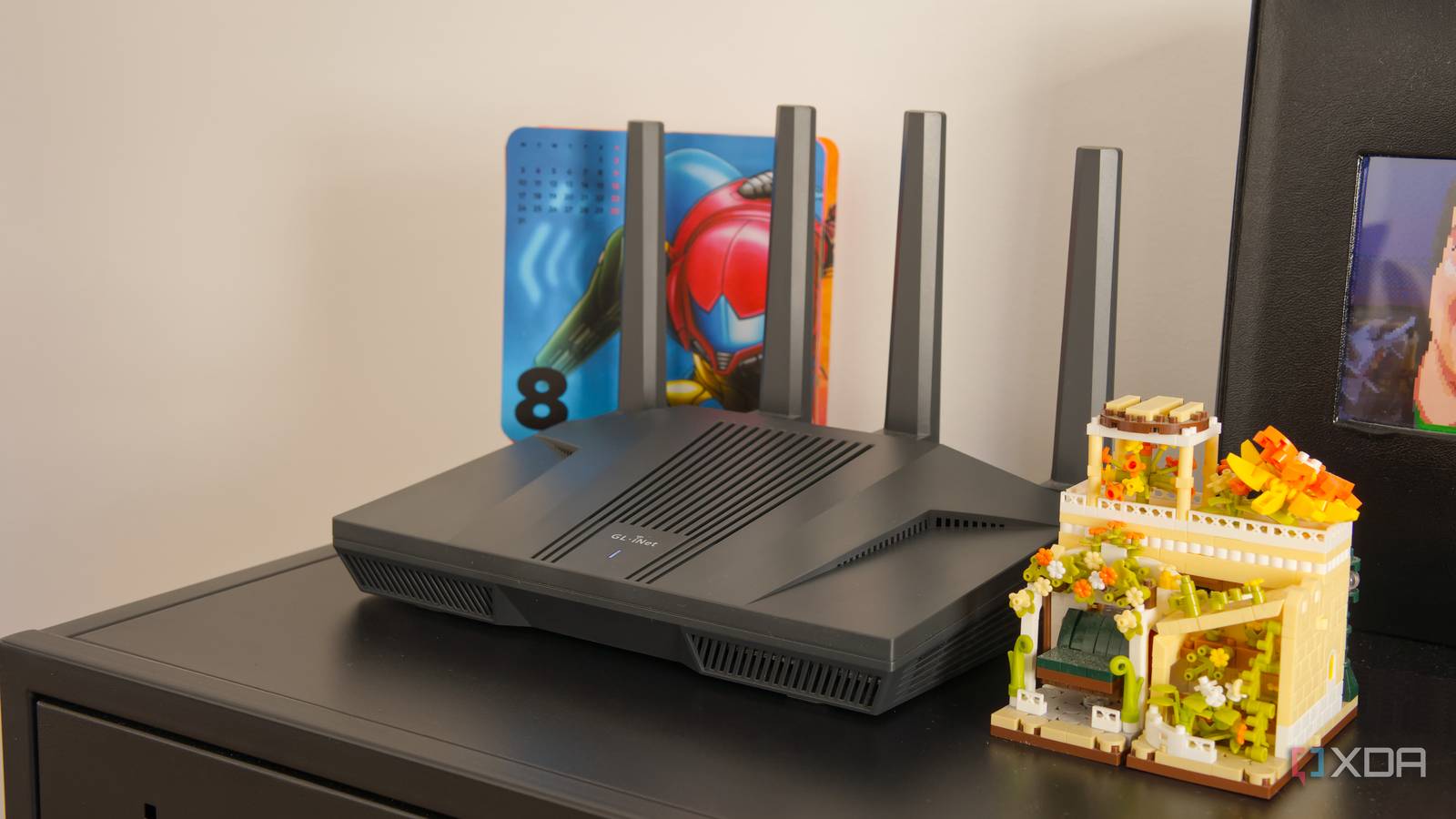 A Wi-Fi router on a black shelf with a calendar featuring video game artwork in the background