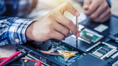 A technician's hand holding a screwdriver at a laptop