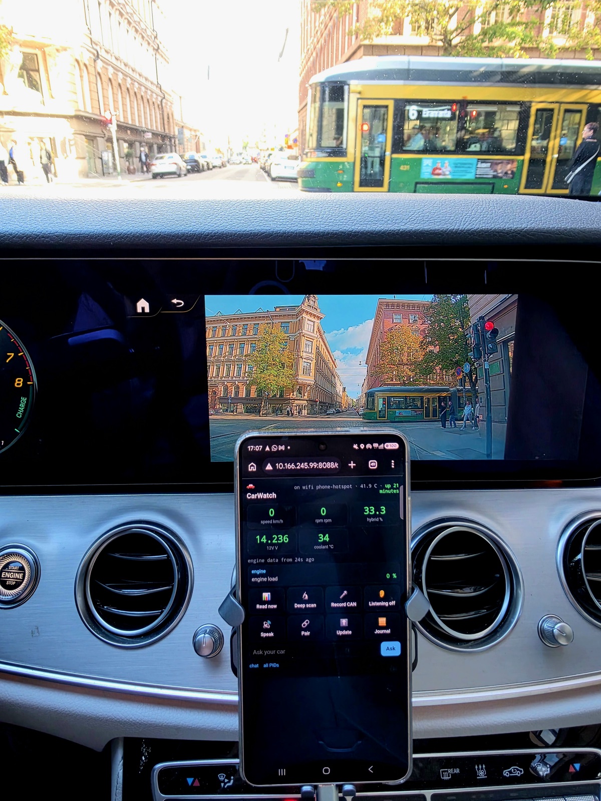 Phone in a Mercedes showing CarWatch live: 0 km/h, 0 rpm, 33.3 percent hybrid, 14.2 V, parked on a Helsinki street