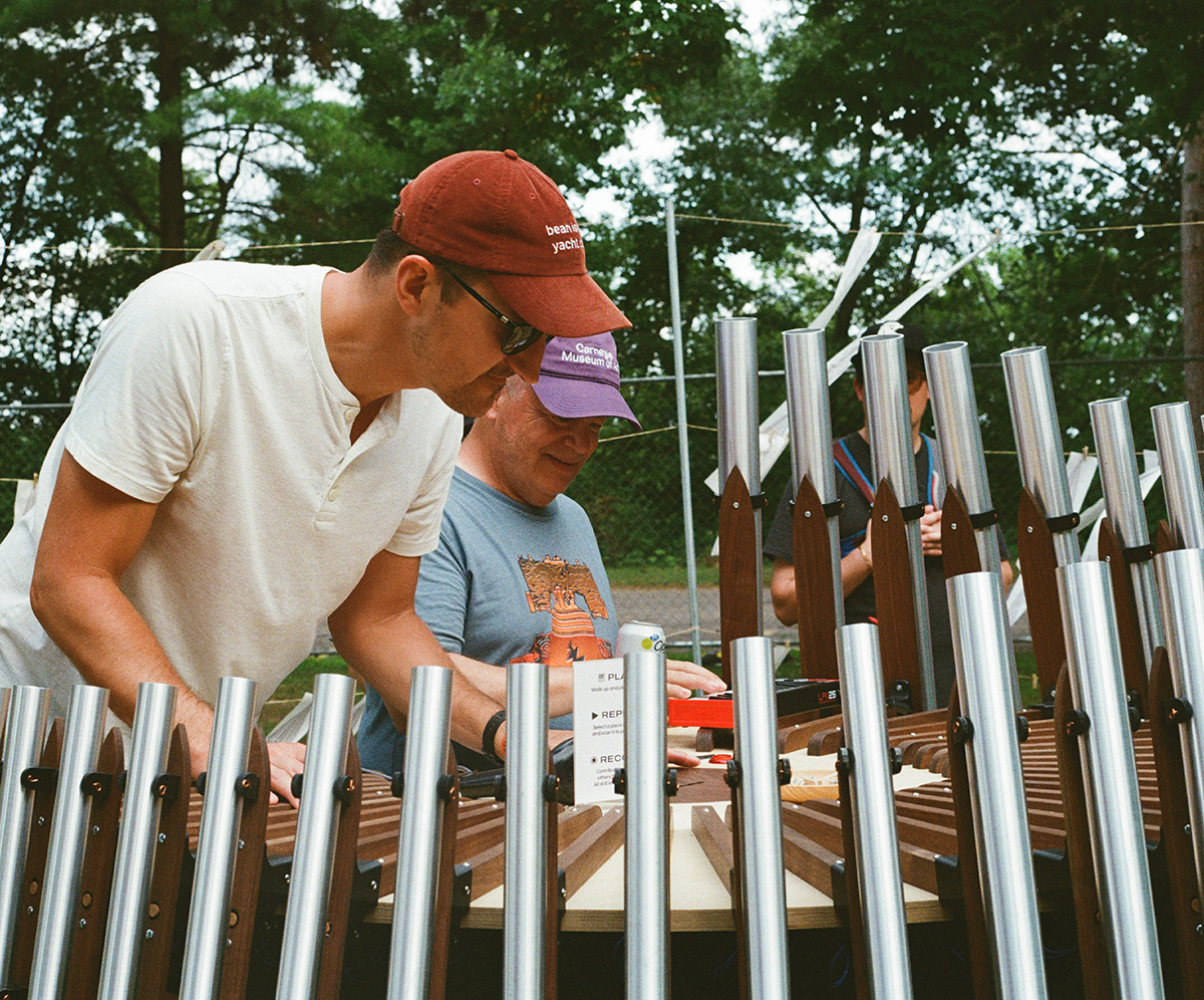 An art installation with many aluminum tubes arranged around the performer. Ben Holmen and another man are inspecting it. Photo by Evelyn Nelson.