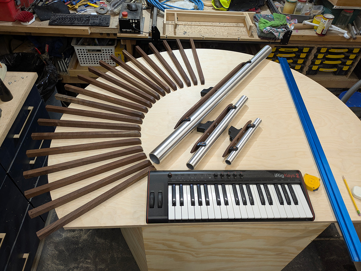 An arrangement of the core components of the instrument: walnut rays radiating from a center point, birch plywood, aluminum chimes, walnut supports, and a MIDI keyboard
