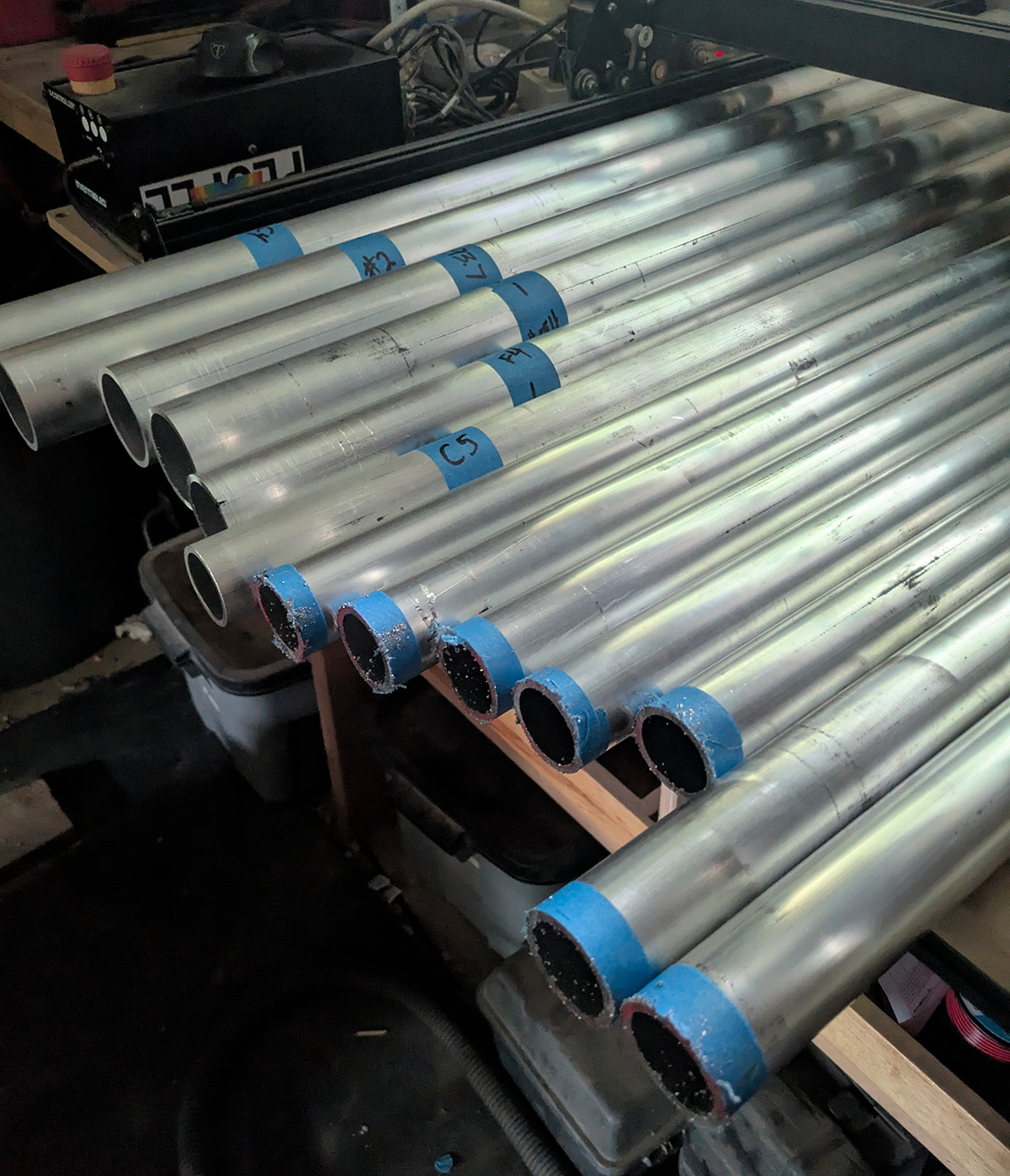 A pile of aluminum pipe is sitting on a work table. They're arranged by length and cut roughly.