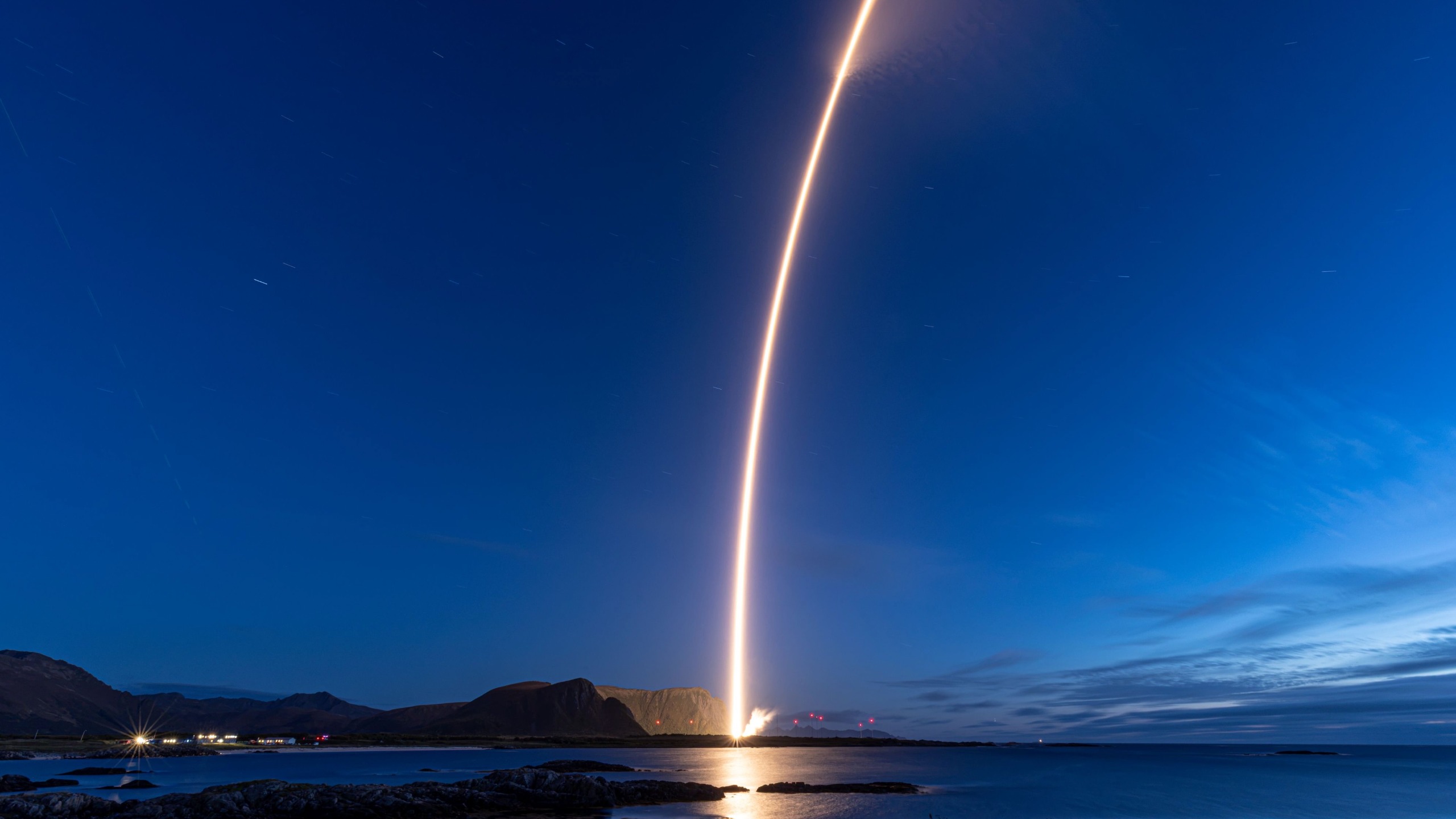 A rocket launch carves an orange arc into a dark night sky in this long-exposure photo.