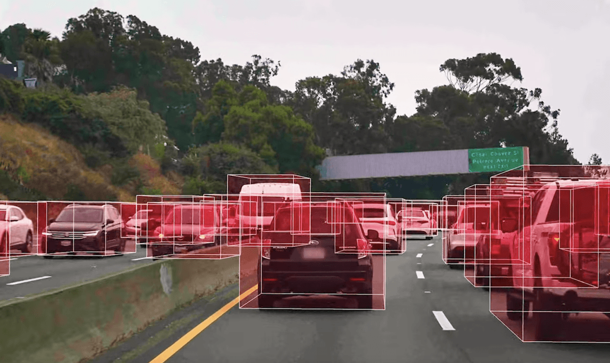 A road scene, shot from the perspective of a driver, shows red splotches to indicate where nearby vehicles were detected using lidar technology developed by Rivian.
