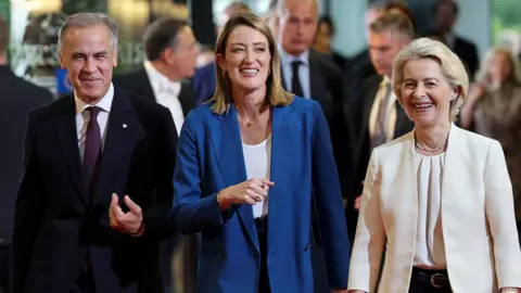 EPA A smiling Mark Carney, wearing a suit, walks alongside European Parliament President Roberta Metsola and Ursula von der Leyen at the European Parliament