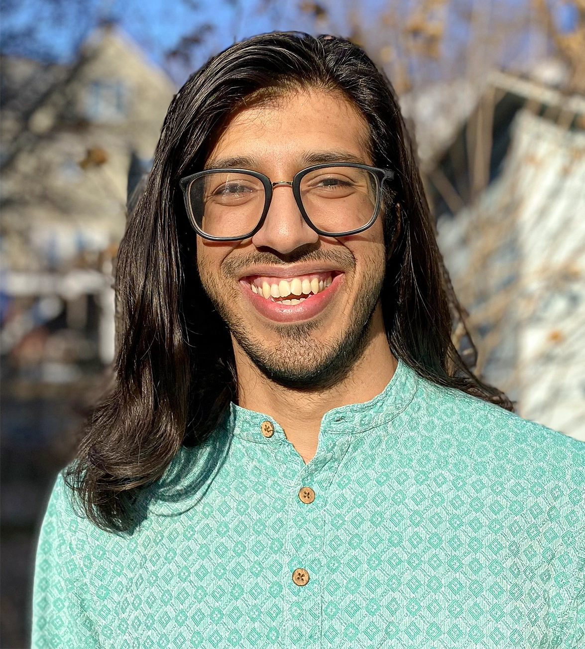 A man in glasses poses outside with houses in the background.